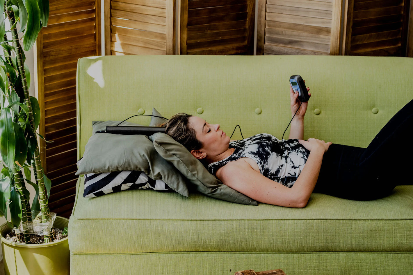 woman laying down on a couch using the biotransducer pro on her head while holding a biomodulator pro 