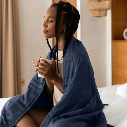 photo of a woman sitting cross legged on a bed holding a cup of coffee with the luna blue throw draped around her 