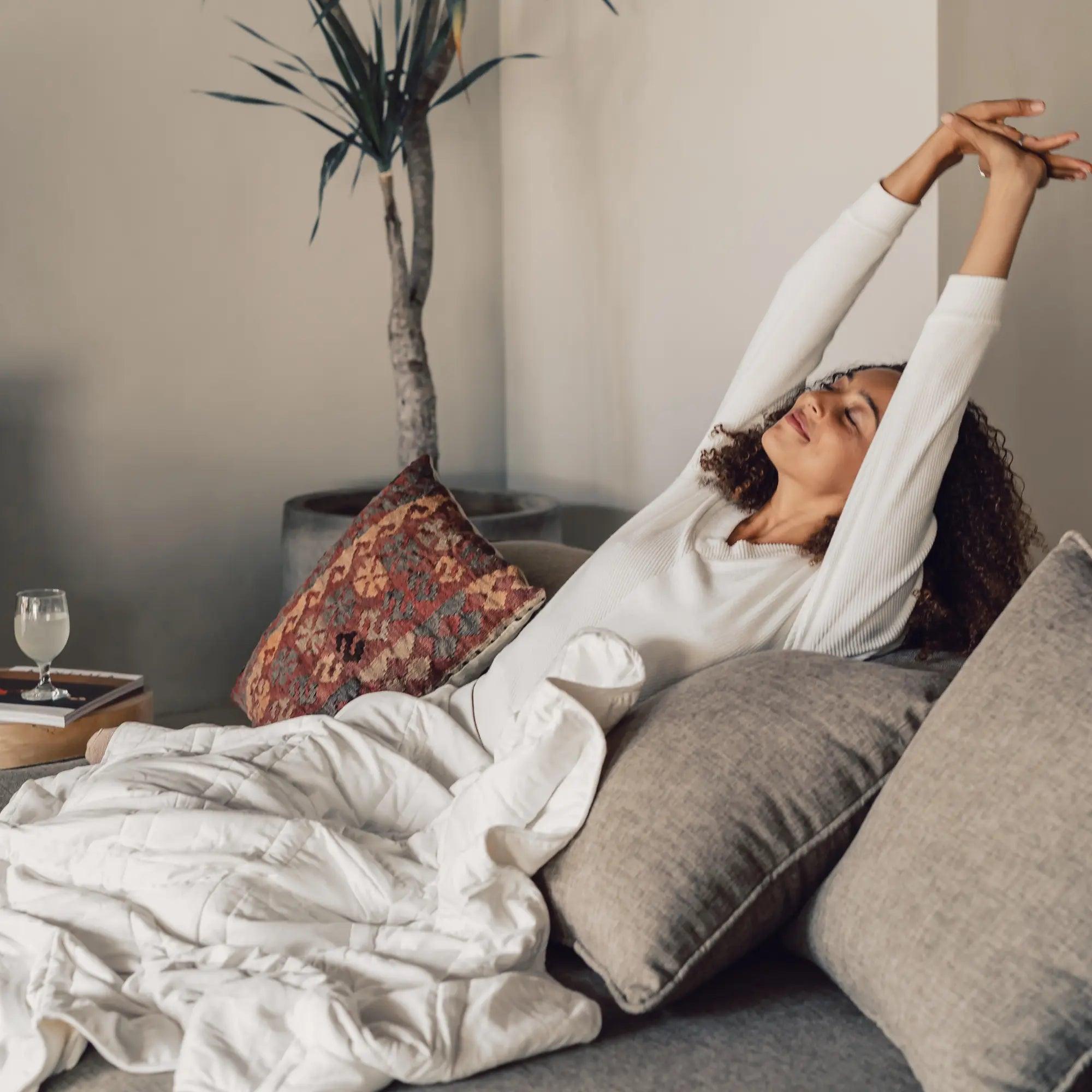 photo of a woman sitting on a couch covered by the pebble white throw blanket 