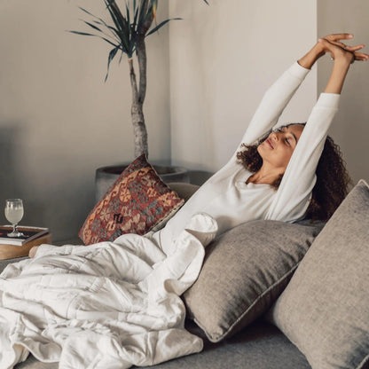 photo of a woman sitting on a couch covered by the pebble white throw blanket 